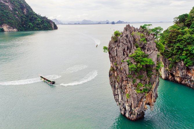 A longtail boat passing the limestone needle of Ko Tapu in Phang Nga Bay